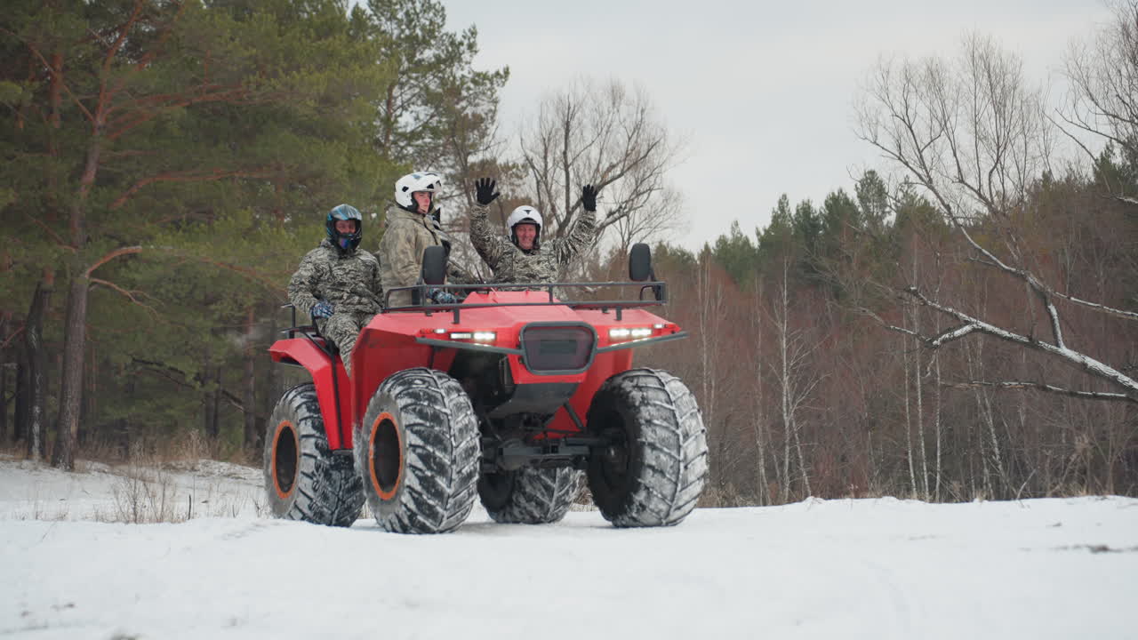 Tre piloti su ATV rossi in inverno, un gruppo che indossa caschi e giacche mimetiche, pneumatici con battistrada robusto che si fanno strada nella neve compatta, il veicolo che attraversa una radura nel bosco, cameratismo energico e lavoro di squadra.