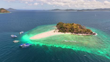 drone hovering over tacling island, with four boats around it, a natural paradise in linapacan, philippines
