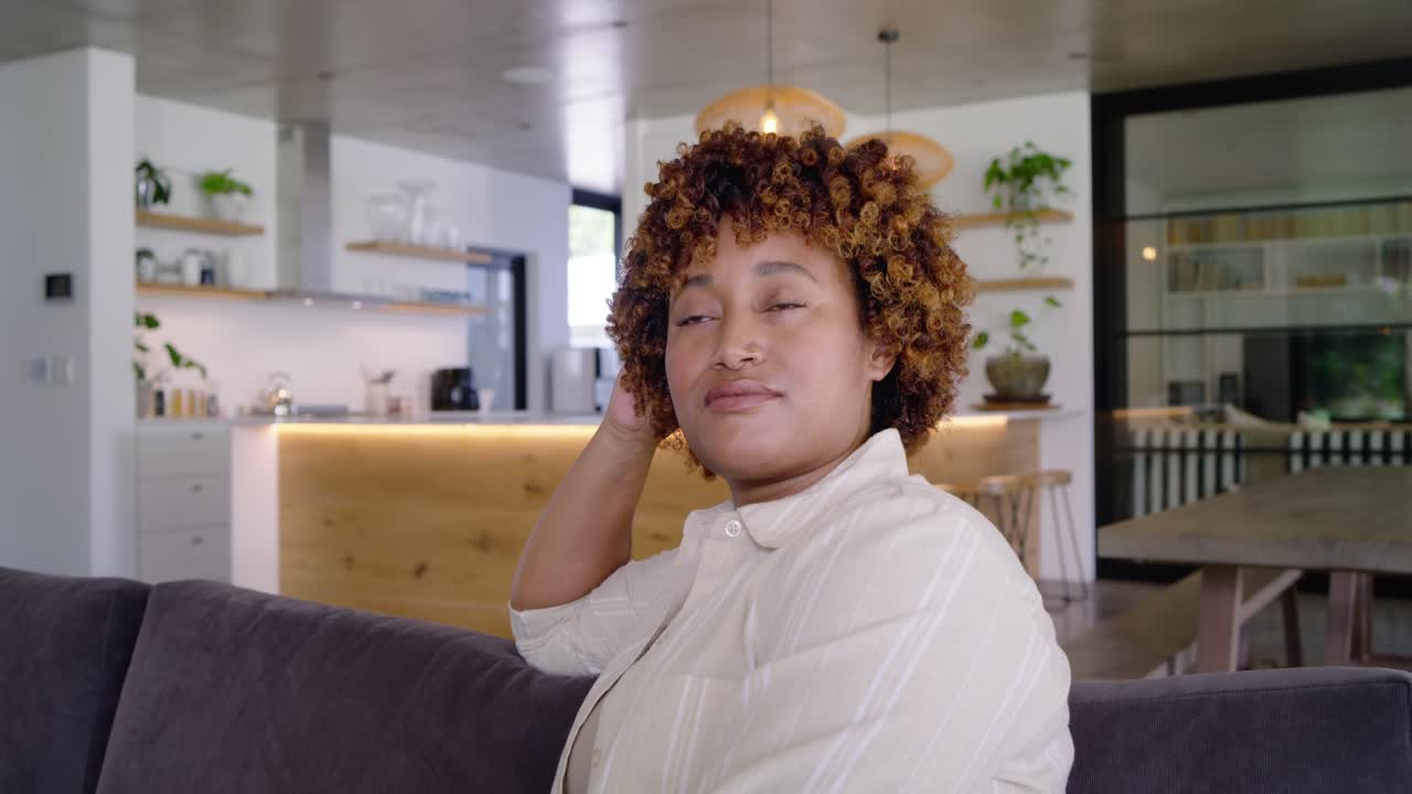 Adult woman reacting off camera touching hair turning head smiling laughing on sofa in open kitchen