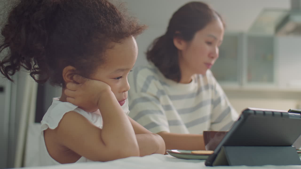 Asian Mother and Little Daughter Using Gadgets during Meal