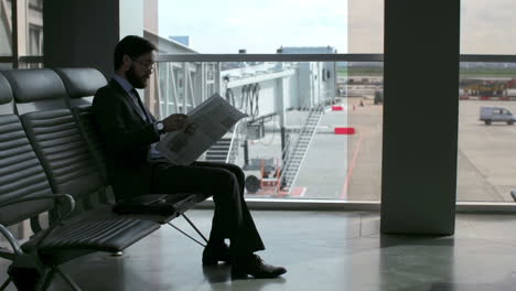 bearded businessman reads a newspaper while sitting at the airport waiting for his flight to depart