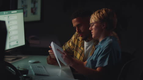 two business colleagues at desks in office working late on computer project together