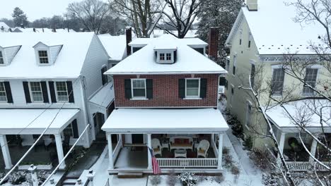 Steigende-Antenne-Des-Schneebedeckten-Hauses-Mit-Amerikanischer-Flagge,-Die-Auf-Der-Veranda-Weht