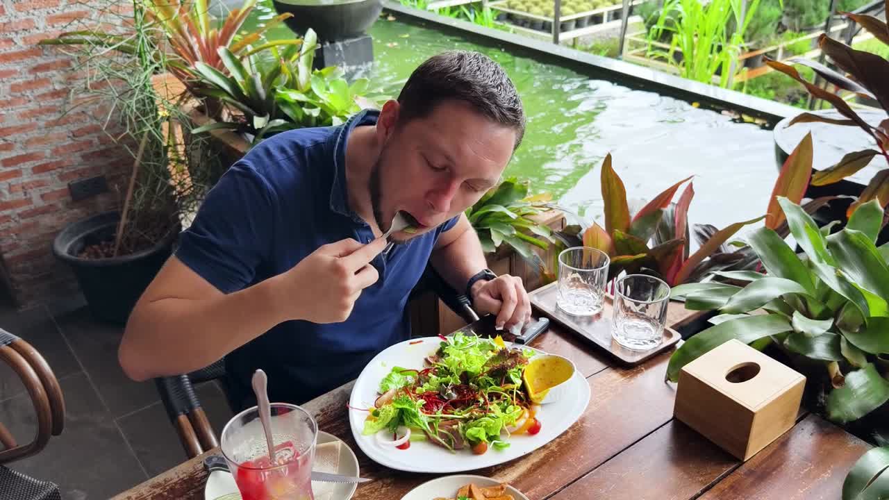 hombre comiendo ensalada en un restaurante al aire libre