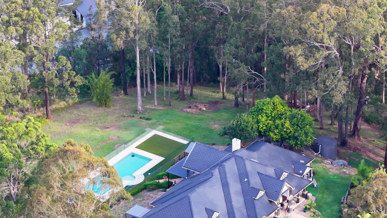 Drone slowly circles modern house, backyard pool, and lush forest in Gold Coast daylight