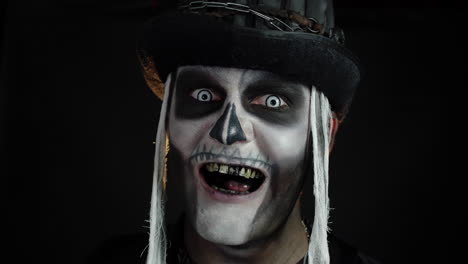 Creepy-man-face-with-skeleton-makeup-in-top-hat-appearing-on-black-background.-Halloween-party