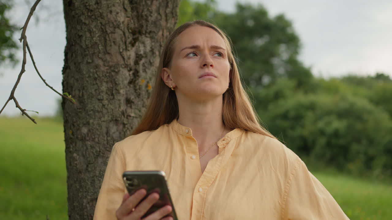 Mujer joven pensando y sosteniendo el teléfono al aire libre