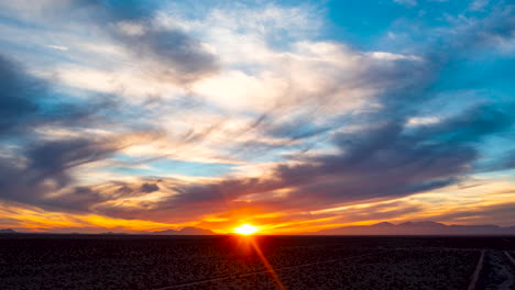 Un-Amanecer-Dorado-Sobre-La-Cuenca-Del-Desierto-De-Mojave-Con-El-Resplandor-Del-Sol-Coloreando-Las-Nubes-Tenues---Hiperlapso-Aéreo-Deslizante