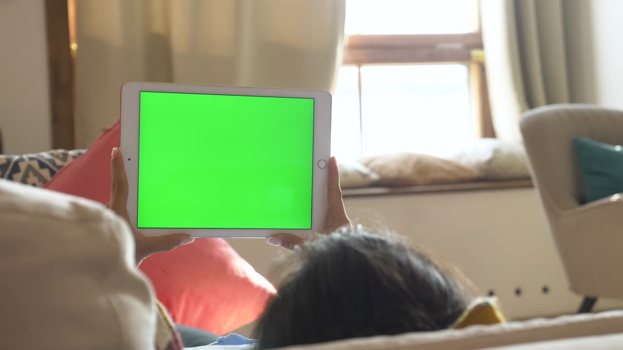 A Young Indian Woman looking on Digital Tablet with Green Screen on Sofa at Home, Horizontal