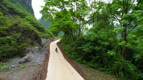 Couple-driving-an-electric-scooter-on-a-winding-road-through-the-lush-landscape-of-Yangshuo,-China