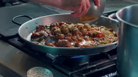 Chef-pours-broth-on-Spanish-paella-with-meat-and-vegetables