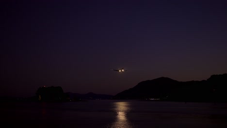 Passenger-plane-landing-above-night-sea,-lights-and-dark