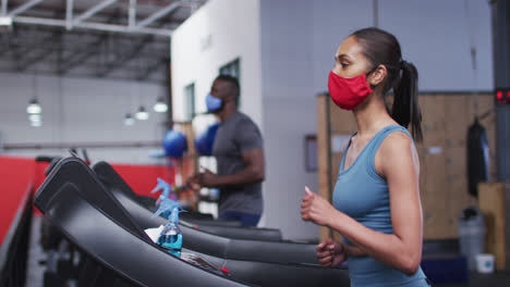 mujer caucásica en forma con máscara facial corriendo en una cinta de correr en el gimnasio