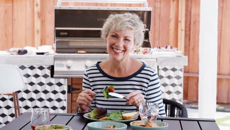 Senior-woman-eating-lunch-in-the-garden-looking-to-camera