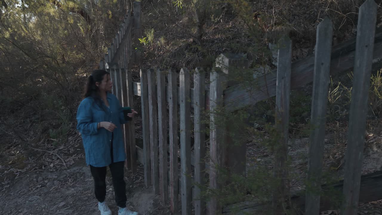Una mujer explora una entrada bloqueada a un túnel histórico en la Montaña Minera Warrandyte, Melbourne. El terreno circundante es accidentado, con luz solar moteada creando una atmósfera misteriosa
