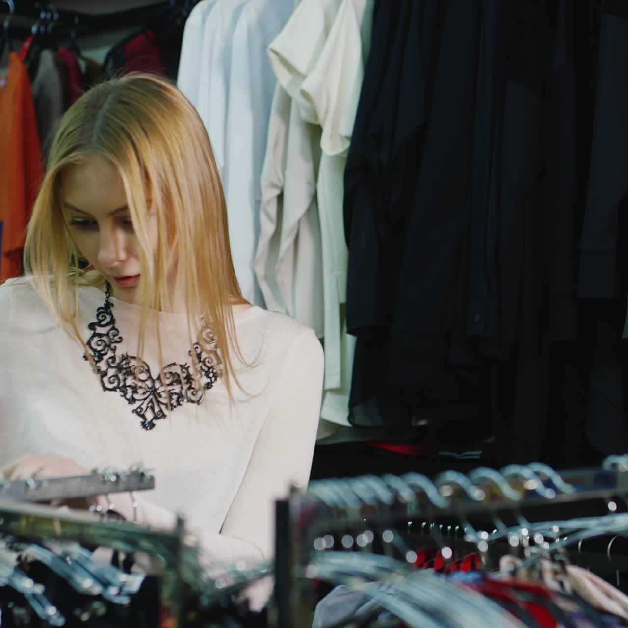 retrato de una mujer joven que elige ropa en una tienda y usa un teléfono inteligente