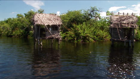 Casas-Con-Techo-De-Paja-Sobre-Pilotes-En-Una-Zona-De-Río-Tropical