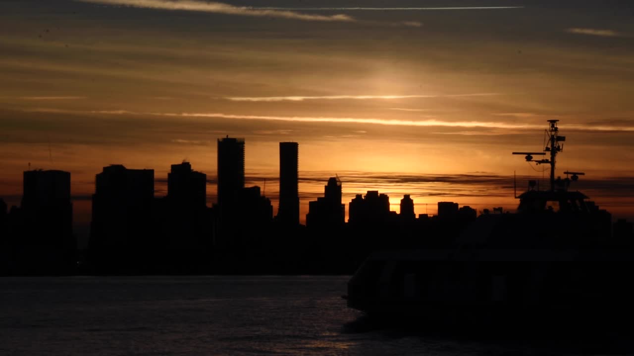 puesta de sol detrás de las siluetas del horizonte de vancouver que dan al cielo un bonito resplandor naranja mientras un ferry de pasajeros navega con sus luces de navegación en el puerto de vancouver