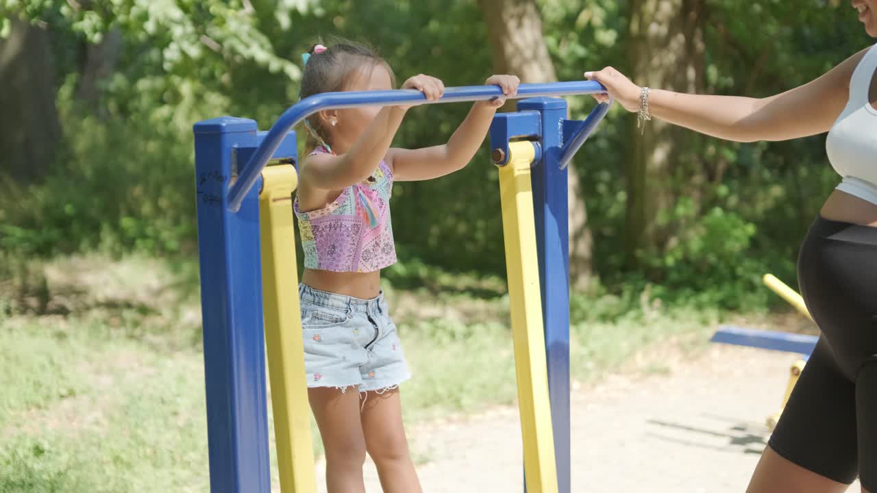 임신 한 어머니 와 딸 이 야외 체육관 에서 운동 하고 있다