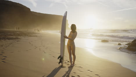 woman with surfboard on a sunset beach