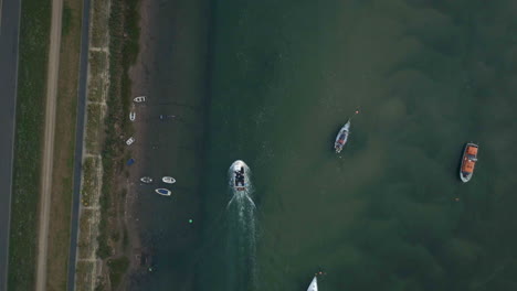 top down drone shot of small working fishing boat travelling through creek harbour with other small sailing boats on uk east coast