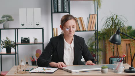 Businesswoman-working-on-laptop-meditating-doing-yoga-breathing-exercise-in-lotus-position-at-office