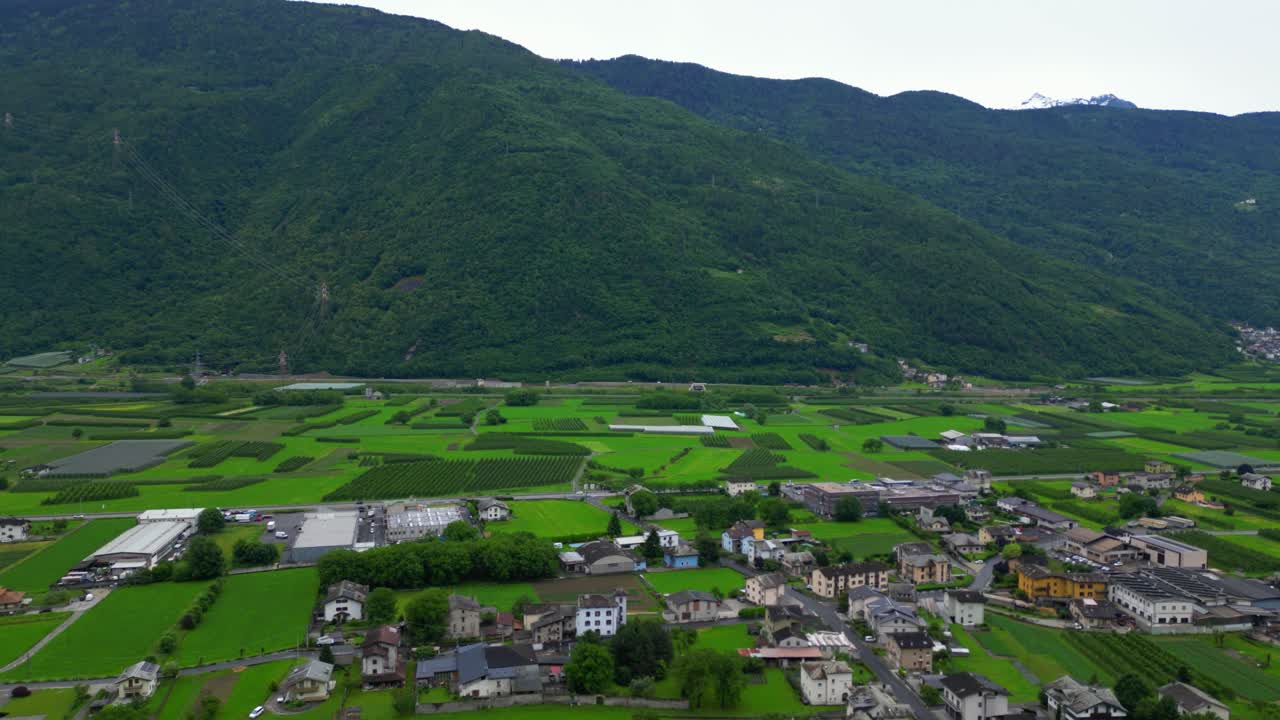 森林に覆われた山々とアルプスの地形に囲まれた広々とした緑の農地の広角ドローンビュー。イタリア、ソンドリオ県のヴィッラ・ディ・ティラーノで撮影 (Italia)。