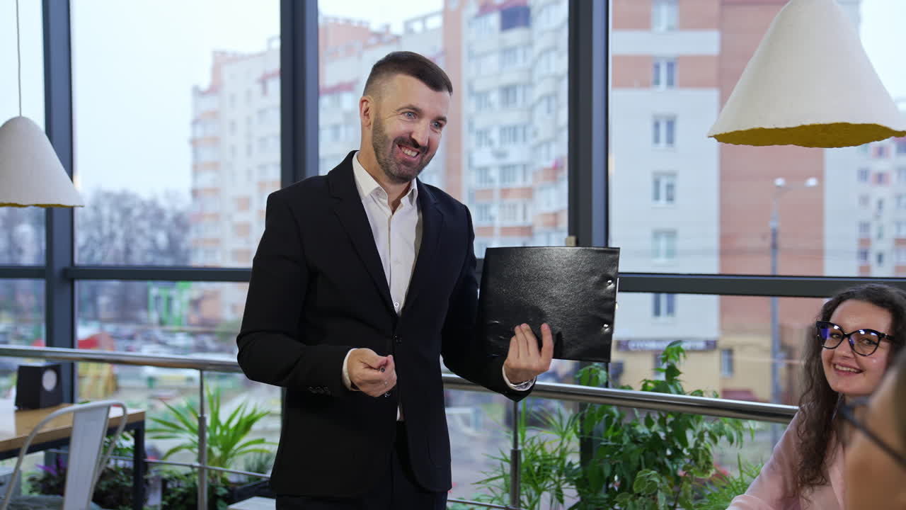 Businessman wearing suit talking to business colleagues or partners sitting at conference table. Male leader holding a folder in his hands showing a chart to his colleagues.