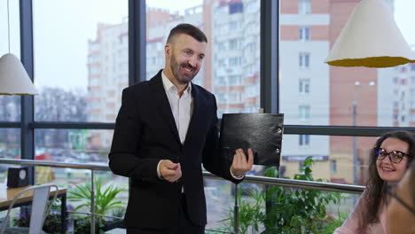 businessman wearing suit talking to business colleagues or partners sitting at conference table. male leader holding a folder in his hands showing a chart to his colleagues.