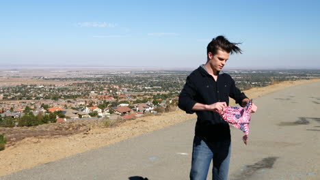 A-young-attractive-man-smiles-and-waves-a-red-white-and-blue-american-flag-bandana-in-slow-motion-on-a-high-desert-ridge