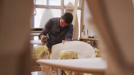 caucasian male surfboard maker working in his studio and making a wooden surfboard