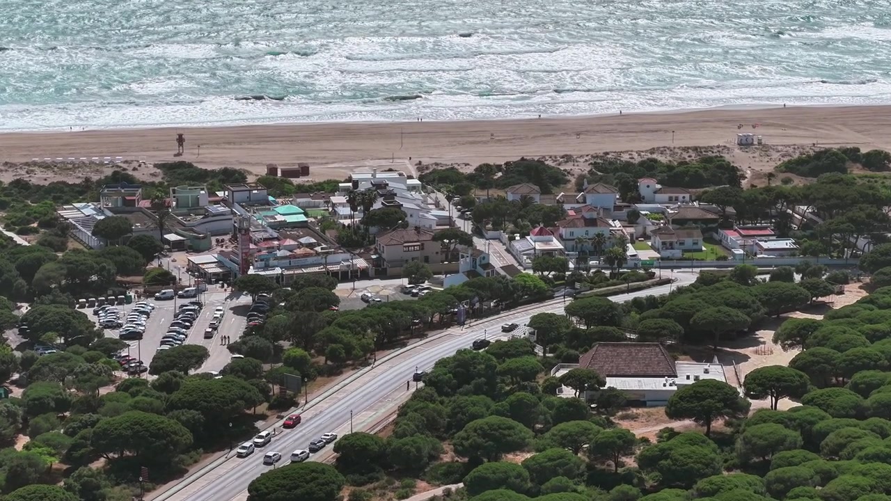 Vista aerea che mostra l'Oceano Atlantico che incontra la costa con sviluppo urbano, strada e alberi verdi. Carrellata aerea in avanti.