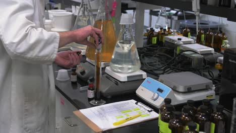 científico en bata de laboratorio mezclando productos químicos en una botella de vidrio en un laboratorio