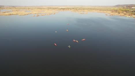 Kayakers-paddling-on-a-serene-lake-under-a-clear-sky,-aerial-view