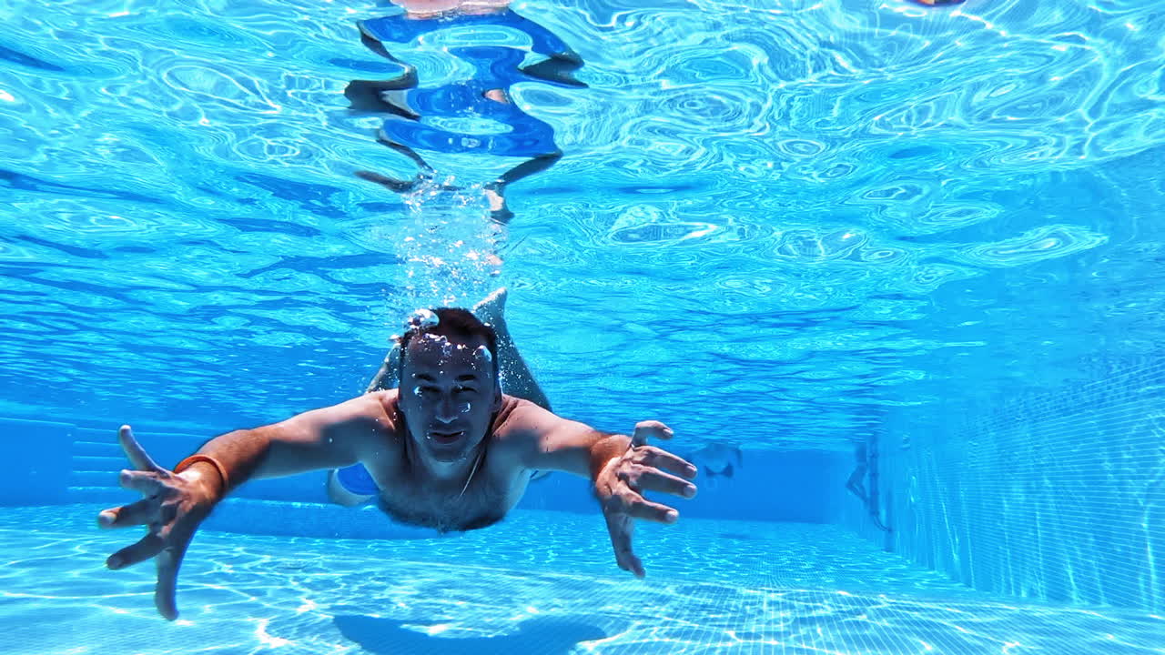 Vacation concept. Happy young man swimming inside the swimming pool. Man is diving under the water and moving forward to camera.