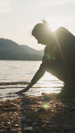 la mujer toca la superficie del agua al atardecer. la dama lleva la mano sobre el agua en los cálidos rayos dorados del sol en la noche de otoño. momento de relajación en la orilla del río y esperando el amor