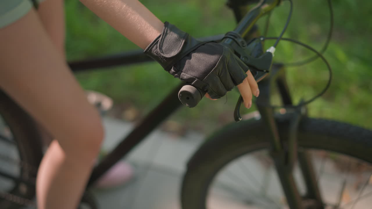 primer plano del manillar de la bicicleta individual con la mano con guante, acelerando y sosteniendo la palanca del freno con precisión, la luz del sol se refleja sutilmente en el guante de cuero, el fondo presenta un desenfoque de vegetación