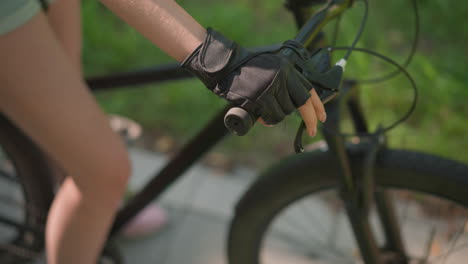 close-up of individual gripping bike handlebar with gloved hand, throttling and holding brake lever with precision, sunlight subtly reflects off leather glove, background features blur of greenery