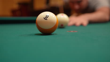 Man-Playing-8-Ball-Pool-Gets-Down-and-Shoots-Striped-Yellow-Nine-Ball-into-Pocket-Past-Camera-using-Draw-or-Backspin-and-Wooden-Cue-Stick-on-Brunswick-Table-with-Green-Felt,-Playing-Billiard-Bar-Games