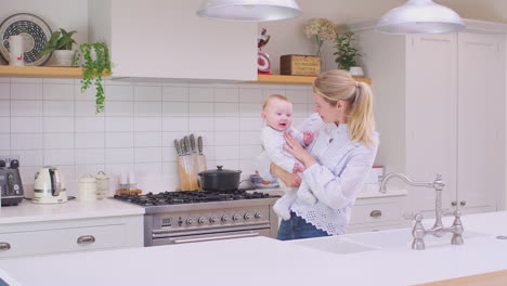 Madre-Amorosa-Llevando-A-Su-Hijo-Riendo-Alrededor-De-La-Cocina-En-Casa-Jugando-Juntos