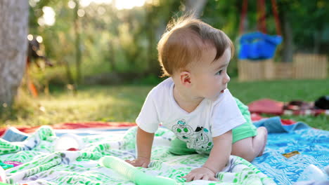 cute baby boy in light clothes crawling by the cloth on the ground. summer time outdoors. blurred backdrop.