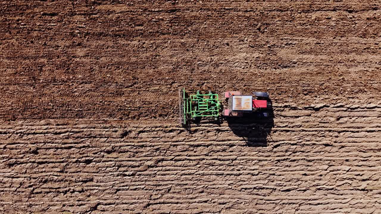 Ripresa aerea di mezzogiorno che segue un trattore di lato attraverso un campo arato proiettando ombre
