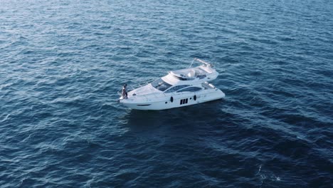 Romantic-Couple-In-Their-Honeymoon-Cruise---Standing-At-The-Bow-Of-A-Yacht-Adrift-In-The-Blue-Sea---slow-orbiting,-aerial