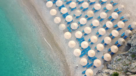 A-view-of-a-beautiful-beach-Chalkos-in-Kythera,-Greece,-full-of-umbrellas-and-blue-sunbeds,-located-by-the-turquoise-sea