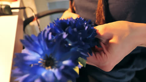 Hands of young woman arrange vibrant blue petals into handmade flower wreath