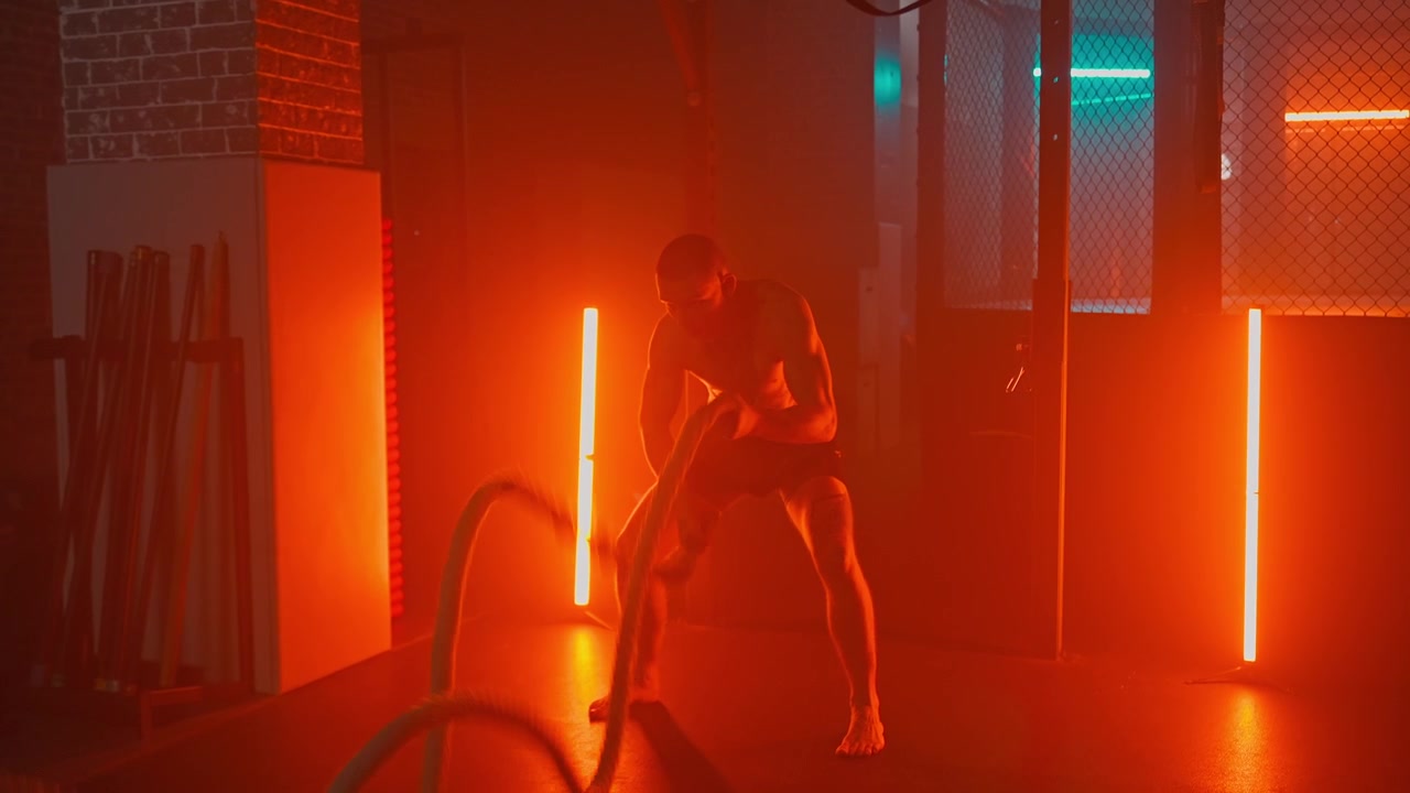 Kraftfull man tränar med battle ropes i dramatisk gymbelysning