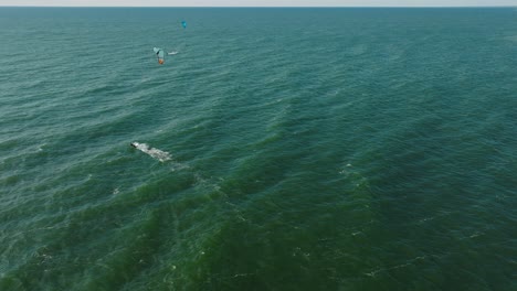 establishing aerial view of a group of people engaged in kitesurfing, sunny summer day, high waves, extreme sport, baltic sea karosta beach , wide drone shot moving forward, tilt down