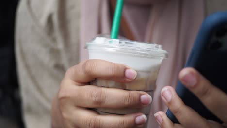 closeup of a woman holding a cup of iced coffee and a phone