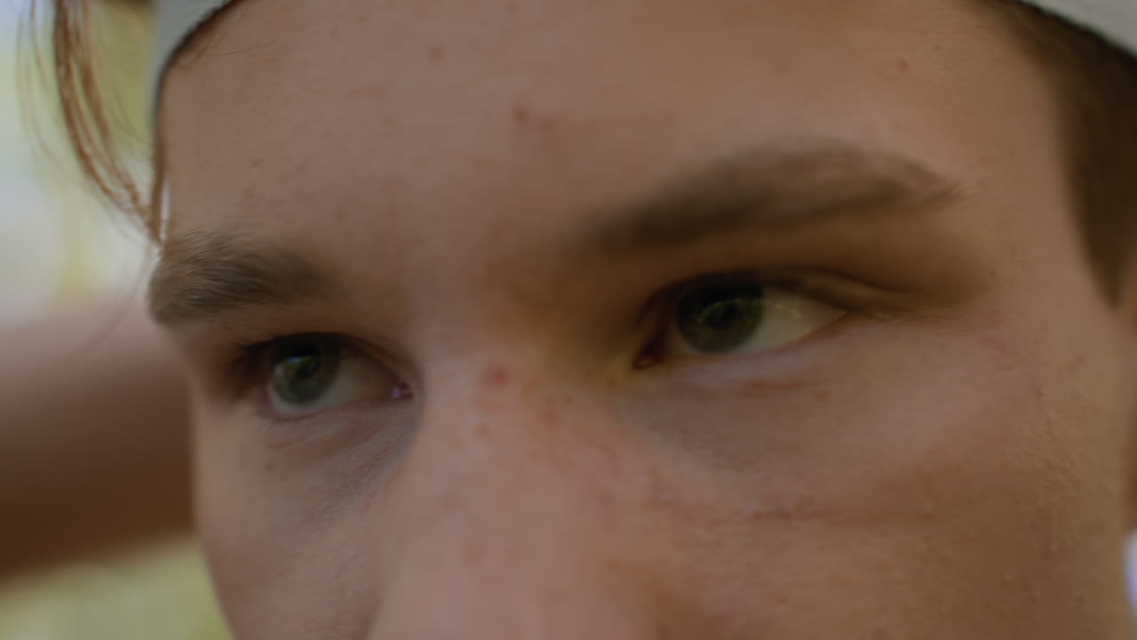 Close up view of soldier showing alertness while tying white headband, sharp focused eyes and furrowed brow, freckles and sweat on skin, blurred woodland background under dappled sunlight