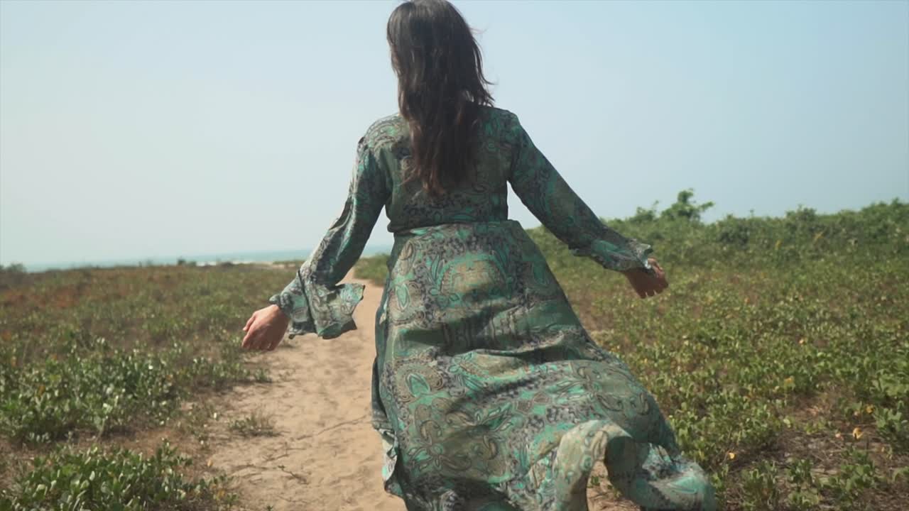 cámara lenta cinematográfica de una chica yogui caminando por un camino de tierra con un vestido que fluye con el viento soplando